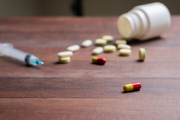 Scattered Pills and Syringe on Wooden Table