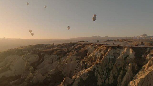 Cinematically flying on a drone over tuff rocks of Cappadocia and approaching a viewpoint with cars and people watching hot air balloons in Cappadocia at sunrise