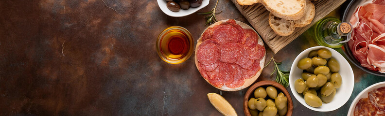 A banner featuring a variety of charcuterie items, sliced meats, olives, bread, and condiments on a rustic wooden table. The arrangement highlights the rich colors and textures of these seasonal items