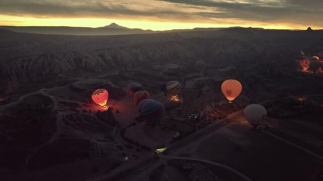 Drone view at twilight over hot air balloons glowing as they inflate with hot air in Rose Valley near G&ouml;reme at sunrise in Cappadocia
