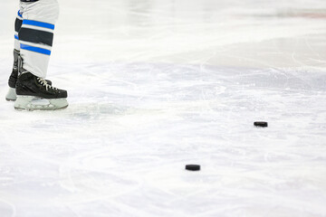 Two hockey black rubber pucks laying on ice with ice hockey playe r staying next.