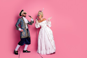 Elegant couples showcasing vintage costumes singing joyfully on a pink background