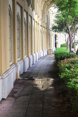 Sidewalk along the house in the shade of trees with a puddle after rain.