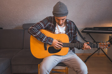 Barefoot musician sits on a wooden chair, fully immersed in playing an acoustic guitar, lost in the...