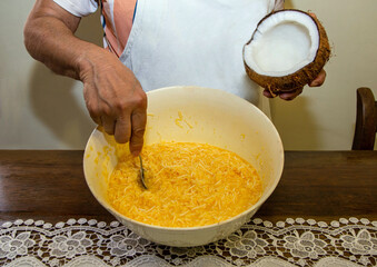 Cook's hands holding an open coconut and stirring dough with grated coconut and eggs to make a sweet called cocada. Cooking concept.