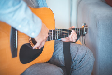 Close-up on musician strums an acoustic guitar in a cozy home, immersed in music. His casual style,...