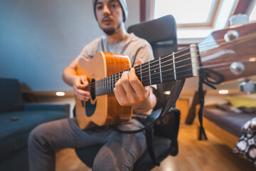 Man alone in the middle of a sunlit room enjoys playing a beautiful wooden acoustic guitar and composing new songs. Immersed in the sweet tones of the guitar. Music that heals the soul