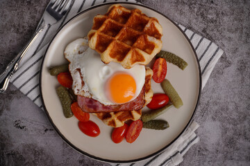 Breakfast waffles with fried eggs Tomatoes and pickled cucumbers In a white plate with a black backgroundBreakfast waffles with fried eggs Tomatoes and pickled cucumbers In a white plate with a black 