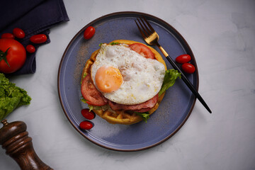 Fresh waffles with fried eggs, lettuce, tomatoes and served for breakfast on a flat table.
