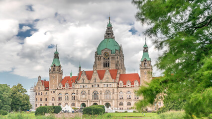 Obraz premium Hyperlapse of Hanover's New Town Hall, a landmark castle-like structure surrounded by park and lake under a cloudy sky. Germany