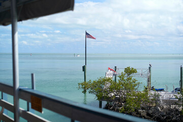 American flag waving by a dock overlooking calm ocean waters under a partly cloudy sky, Florida Keys, USA