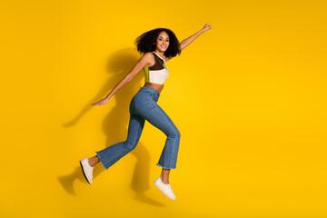 Bright and vibrant scene of a cheerful young woman jumping enthusiastically against a vivid yellow...