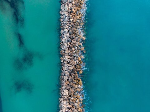 Aerial view of rocky breakwater in turquoise waters.