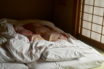 Cozy futon bed with rumpled white sheets in a traditional Japanese room, Japanese Alps, Shiba Onsen