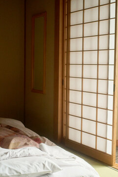Cozy bedroom with traditional shoji screen and unmade futon bedding in soft light, Japanese Alps, Shiba Onsen