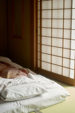 Sunlight filters through a shoji screen, illuminating a neatly made Japanese futon on tatami mats, Japanese Alps, Shiba Onsen