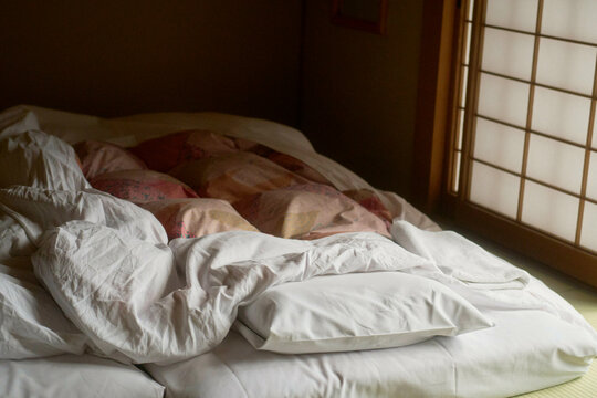 Cozy futon bed with rumpled white sheets in a traditional Japanese room, Japanese Alps, Shiba Onsen