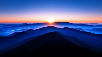 Obraz premium A stunning sunrise illuminates misty mountains, casting a soft glow over the serene landscape, blending shades of blue and orange.