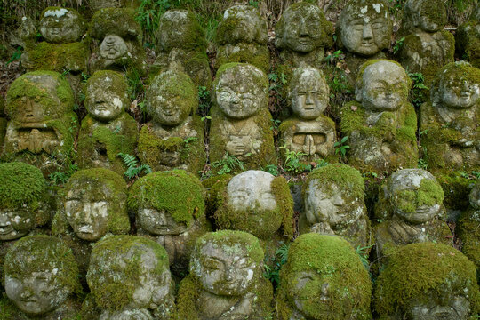 Stone statues covered with moss, arranged in rows, amidst greenery in a forest setting. Kyoto, Japan