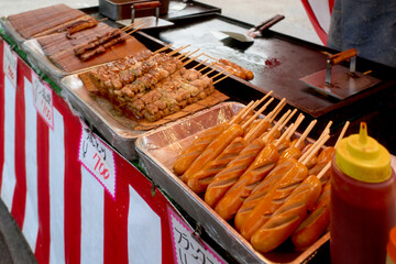 Assorted grilled skewers and corn dogs on a street food vendor's striped counter.  Osaka, Japan