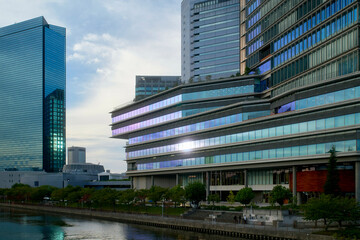Modern urban skyline with reflective glass skyscrapers beside a calm waterfront at sunset. Osaka, Japan