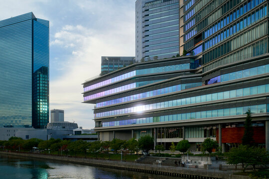 Modern urban skyline with reflective glass skyscrapers beside a calm waterfront at sunset. Osaka, Japan