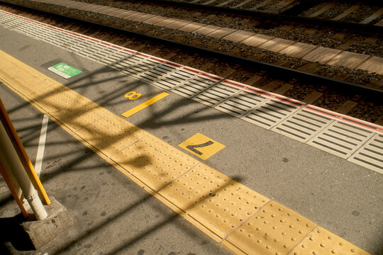 Empty train platform with yellow tactile paving and track shadows on a sunny day. Osaka, Japan