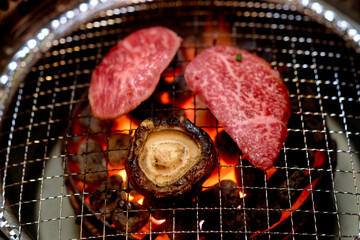 Slices of marbled beef and a mushroom grilling over open flames on a metal barbecue grate. Tokyo, Japan