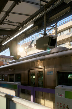 Sunlight illuminates an urban train station platform with a train and surrounding buildings. Tokyo, Japan