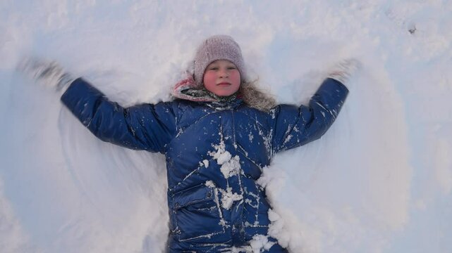 Child makes an snow angel while lying in the snow.