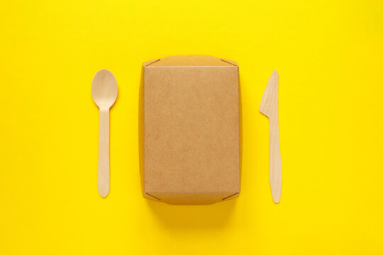 wooden disposable cutlery - knife, tablespoon and container on yellow bachground lunch environmental problem