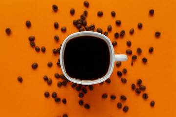 small white cup of black coffee with coffee beans on orange background