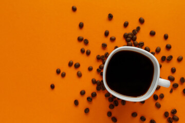 small white cup of black coffee with coffee beans on orange background