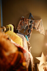 Handcrafted bat costume hanging on wall surrounded by clothes on hangers in cozy, warmly lit room....