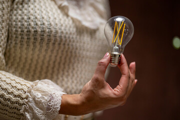 Hands holding an incandescent light bulb against a knitted sweater background. Netherlands
