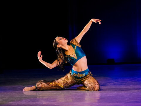 Dancer elegantly poses on stage with vibrant blue and gold costume under dramatic lighting, The Nutcracker, Bainbridge Island, USA