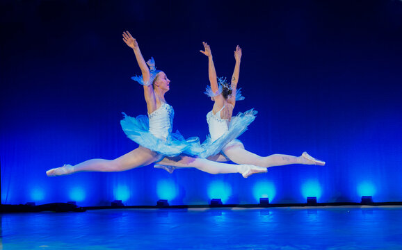 Two ballerinas in blue tutus perform ballet leaps on stage with dramatic blue lighting. The Nutcracker, Bainbridge Island, USA