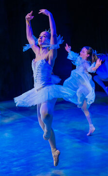 Ballerinas in white tutus perform a graceful dance under blue stage lighting. The Nutcracker, Bainbridge Island, USA
