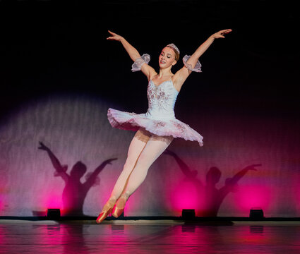 Ballerina in pink tutu performing a graceful jump on stage with colorful lighting. The Nutcracker, Bainbridge Island, USA