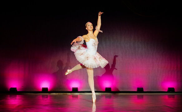 Ballerina gracefully performing on stage in a pink tutu with vibrant lighting. The Nutcracker, Bainbridge Island, USA