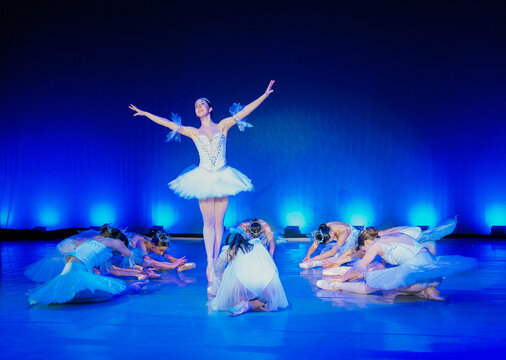 Ballet dancer in a white tutu performs on stage with blue-lit background. The Nutcracker, Bainbridge Island, USA