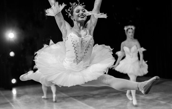 Ballerina performs a graceful leap on stage, wearing a white tutu, with another dancer in the background. The Nutcracker, Bainbridge Island, USA