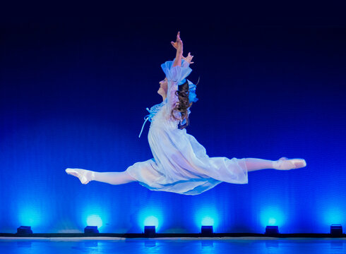 Ballerina in a flowing dress performs a split leap on stage with blue lighting in the background. The Nutcracker, Bainbridge Island, USA