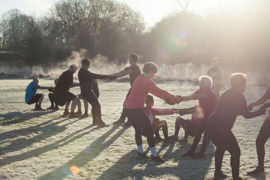 A group of adults engage in a team exercise in a frosty park on a sunny morning, creating a chain through linked arms. Sale Water Park, Manchester, UK