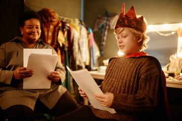 Scene depicting actor wearing crown and cape receiving guidance from mentor in dressing room....