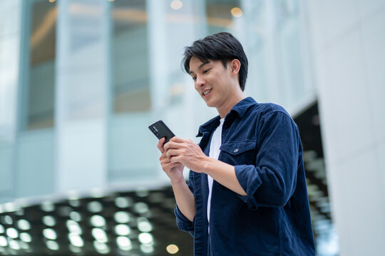 smiling happy successful asian businessman or lawyer in gray suit and blue shirt calling with his phone near his ear standing in front of an office building.Successful businessman holding mobile phone