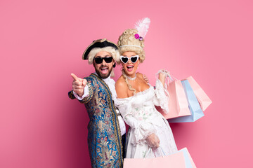 Playful couple in elegant vintage costumes against a retro pink background, sharing laughter with...