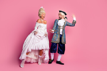 Elegant couple in royal-themed costumes against a pink backdrop at a masquerade