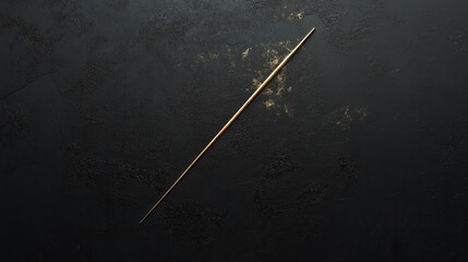 Fototapeta premium Elegant gold stick rests on a textured black surface illuminated by soft light at an artistic angle