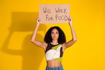 Young woman holding cardboard sign with humorous message against vibrant yellow background, evoking...